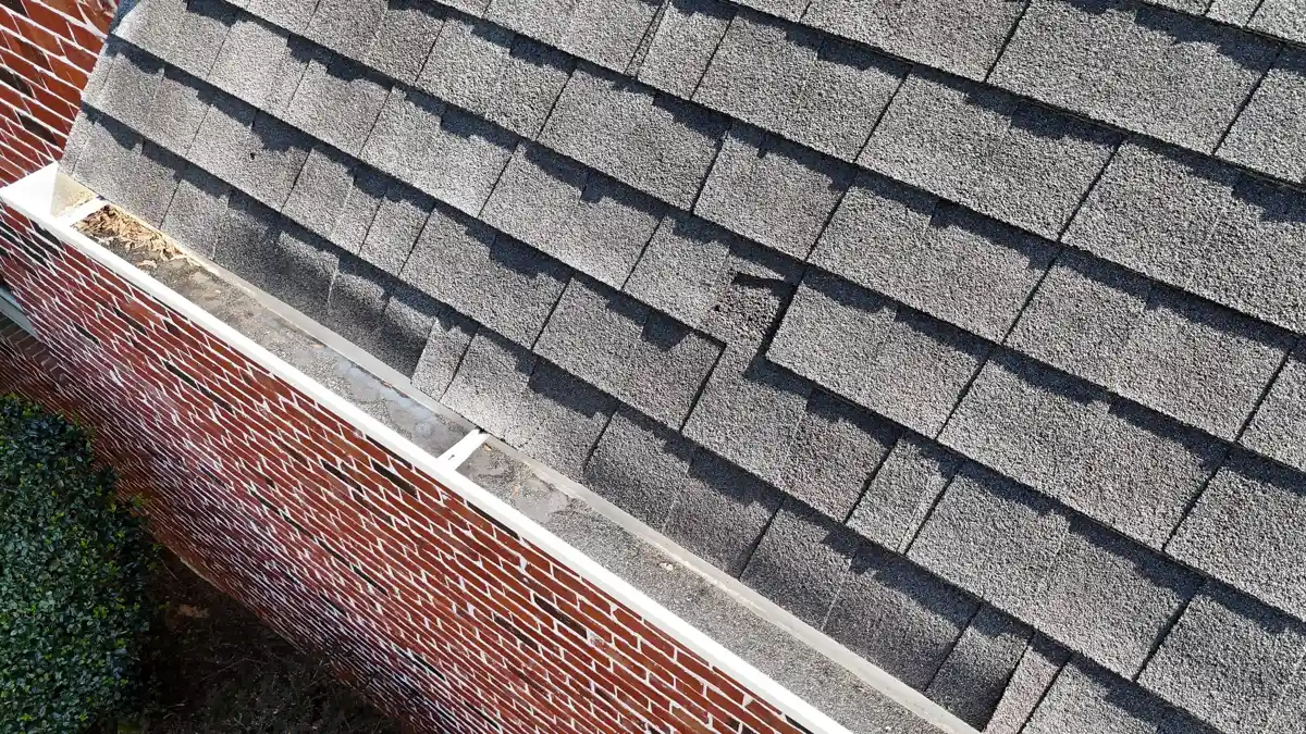 Roof shingles beside white gutter along brick exterior wall, Southern Premier Roofing work near Arcade GA
