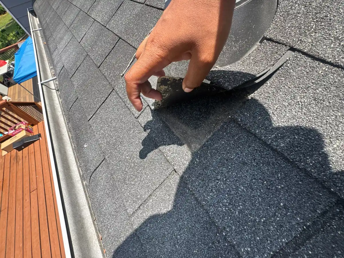 Worker lifting shingle tab beside roof valley and gutter, Southern Premier Roofing work near Auburn GA