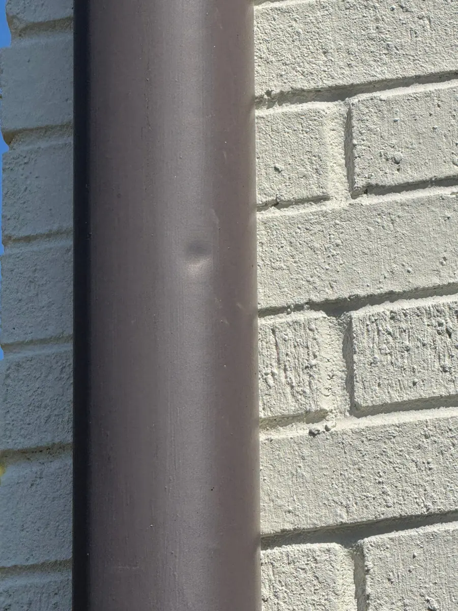 Close-up shows a dented brown downspout beside white brick, Southern Premier Roofing work near Dacula GA