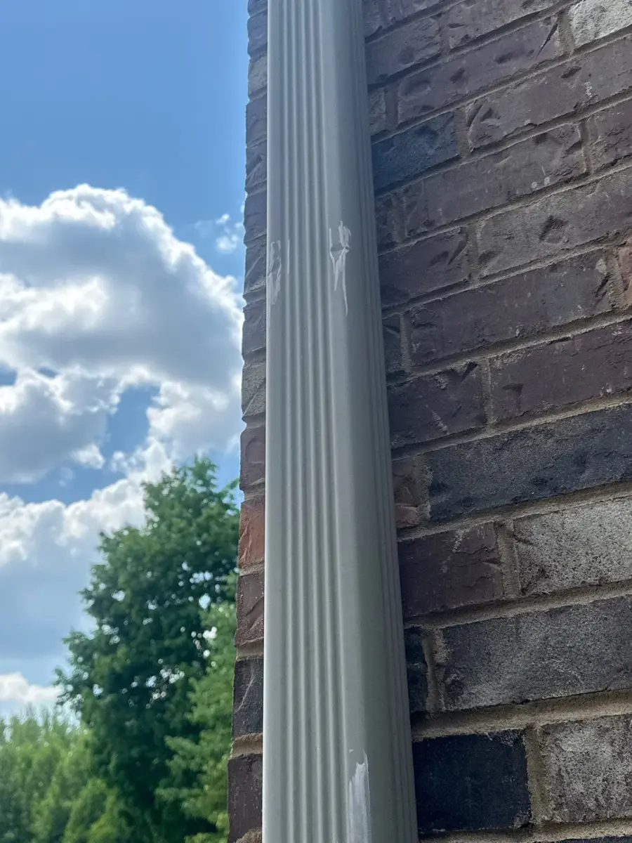 White gutter downspout running beside brick wall under blue sky, Southern Premier Roofing work near Braselton GA