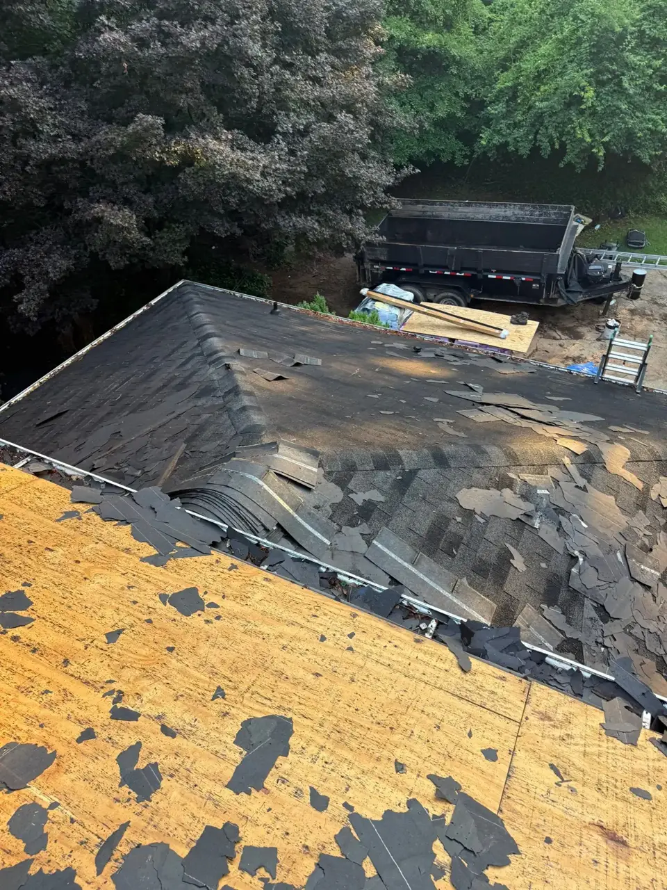 Damaged shingles and exposed roof decking with a dump trailer visible in Athens GA