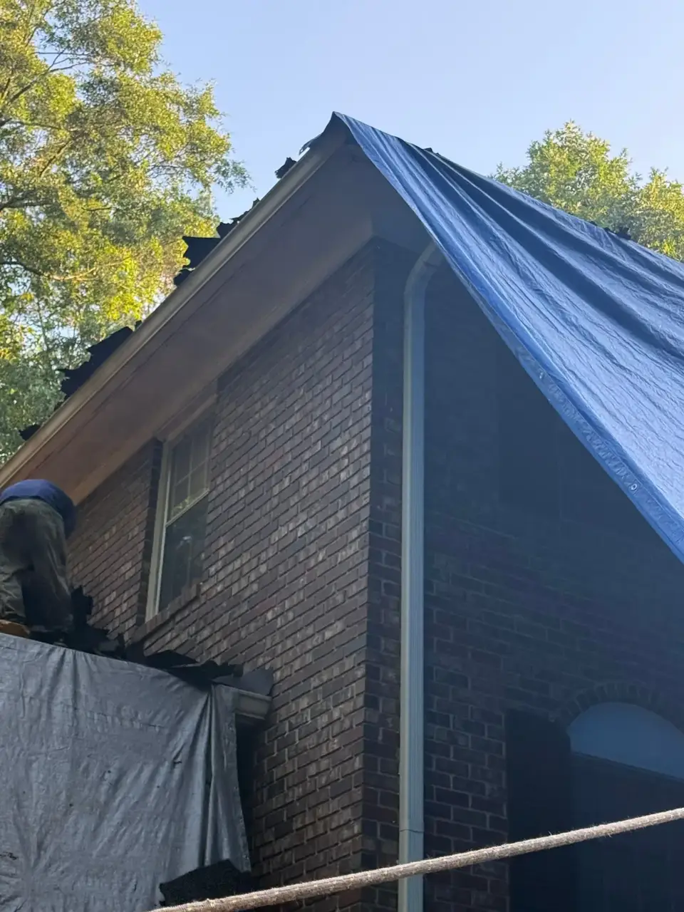 Brick house gable covered by a blue tarp during roof work in Athens GA