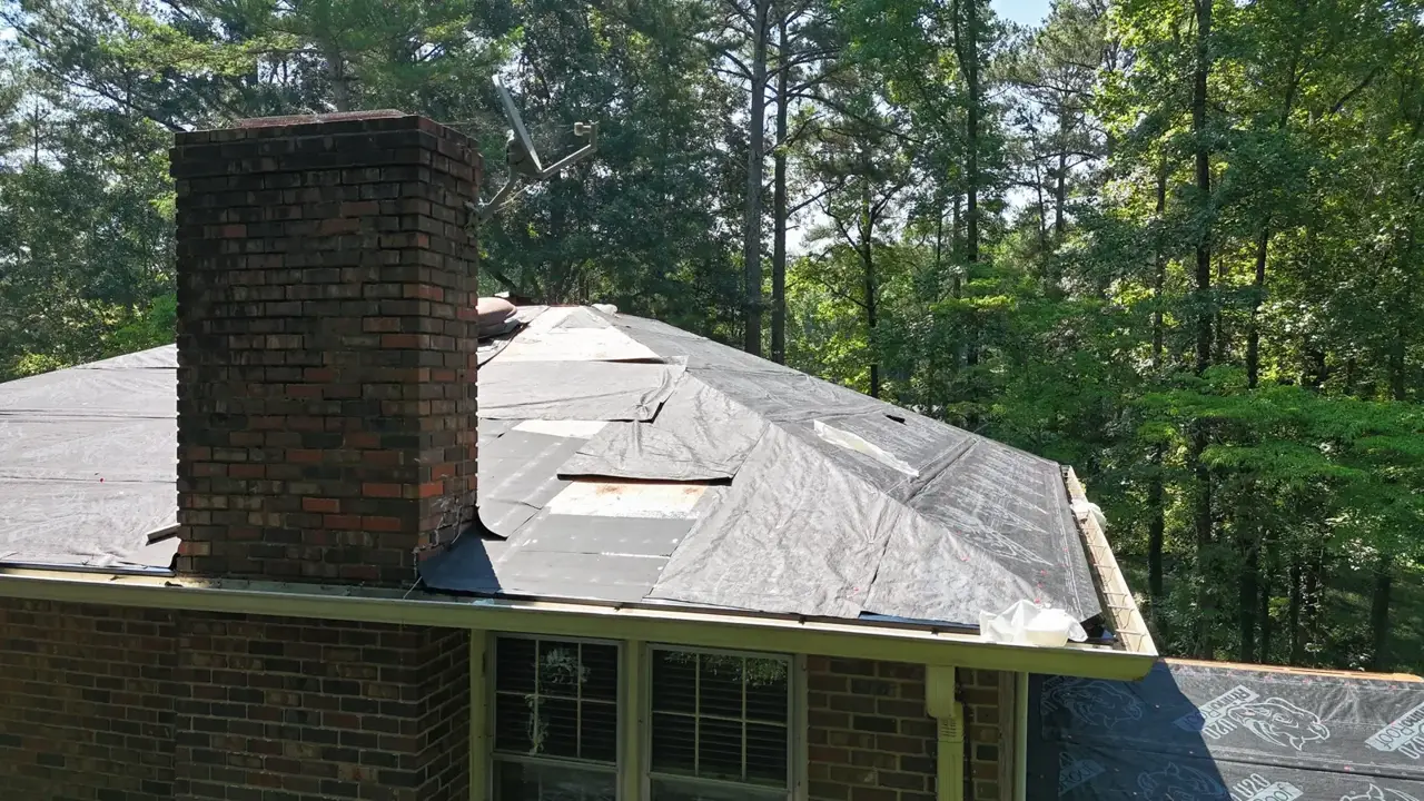 Partially covered residential roof with brick chimney and exposed roof edges among trees