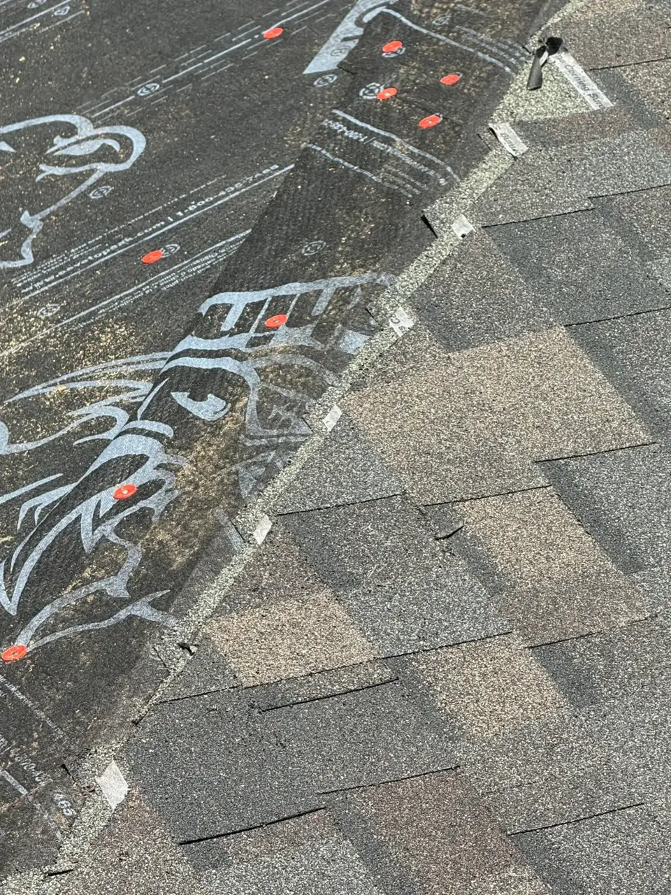 Close view of gray shingles meeting exposed printed roofing underlayment on residential roof