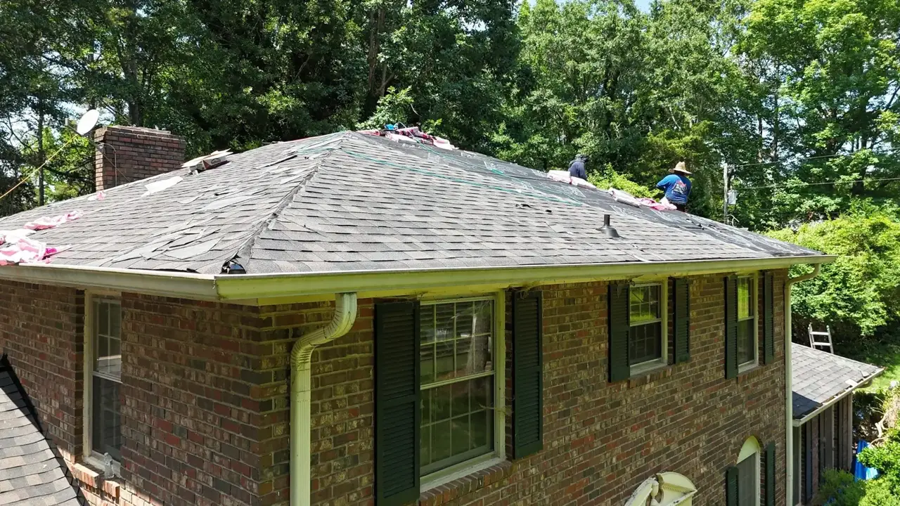 Roof replacement underway on a brick home with workers and exposed shingles in Athens GA