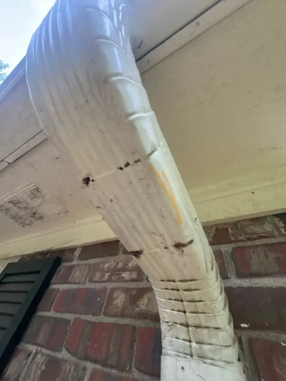Close-up of a weathered white downspout attached to brick siding