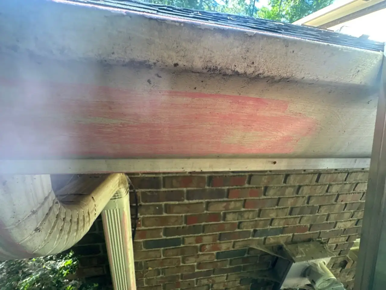 Weathered soffit and gutter downspout above a brick wall in Athens GA