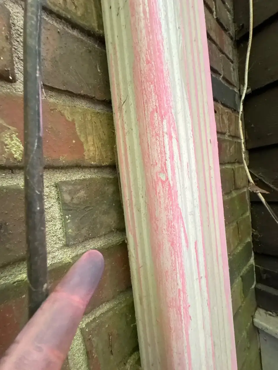 Close-up of weathered painted trim beside brick masonry and a dark vertical cable.