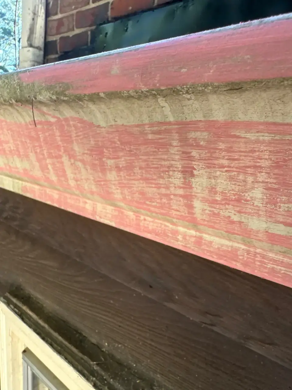 Weathered red-painted exterior trim above dark siding and brick masonry.