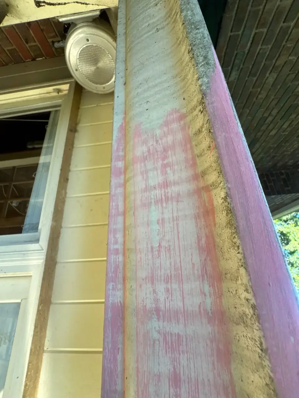 Weathered painted trim beside light siding, a window, and an exterior speaker.