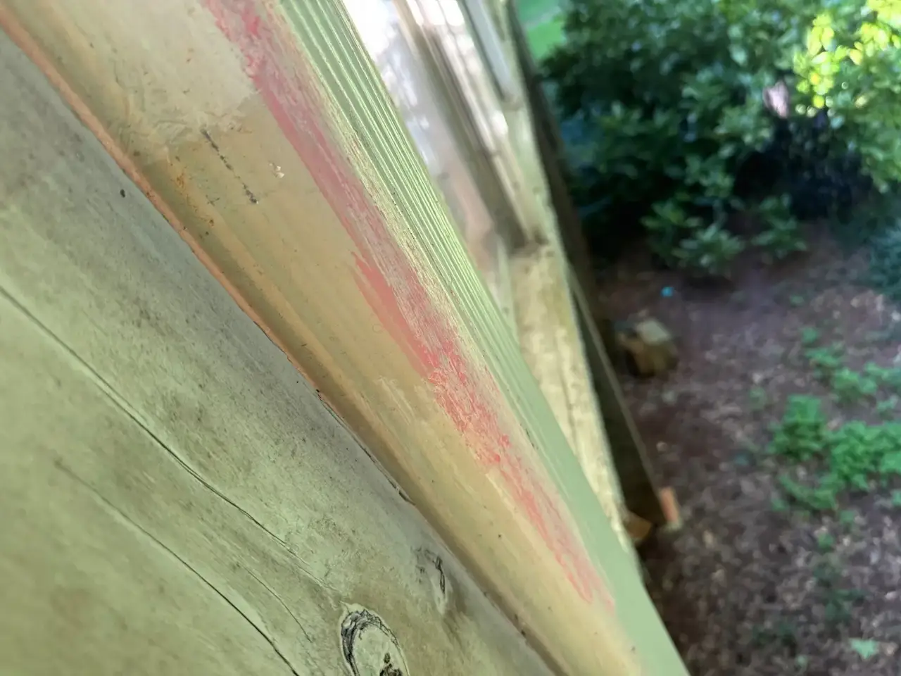 Close-up of weathered painted exterior trim overlooking landscaped ground beside the house in Athens GA.