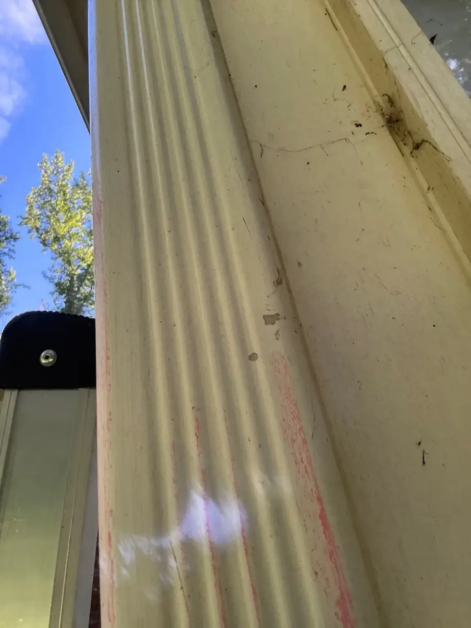Close view of weathered exterior siding beside a dark gutter against blue sky and trees.