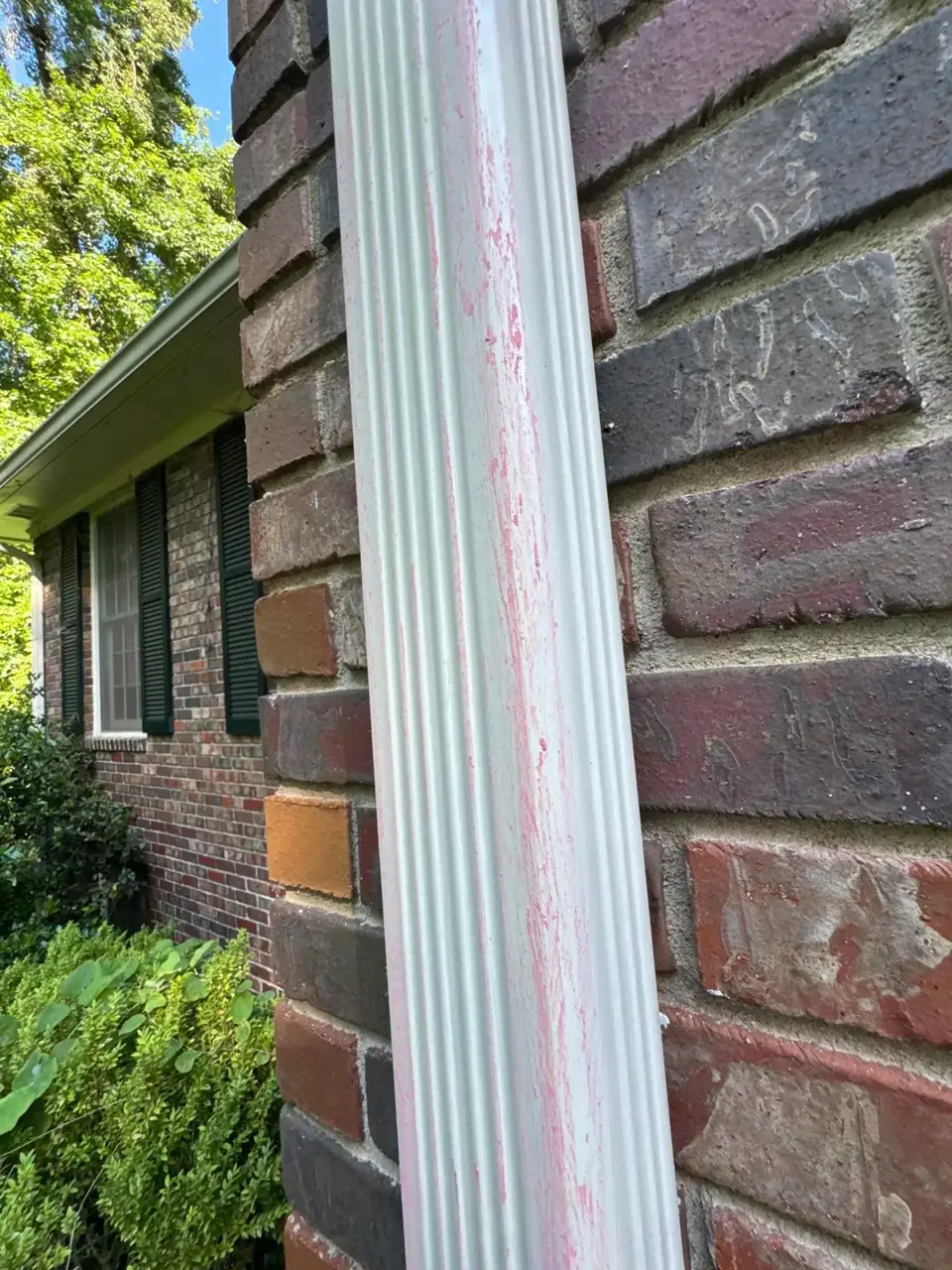 Weathered downspout beside brick wall and window, with landscaping visible in Athens GA.
