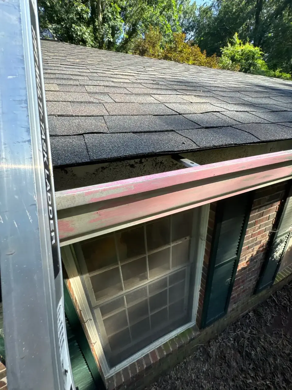 Aged asphalt shingles above brick exterior, with gutter edge, window, and siding visible in Athens GA.