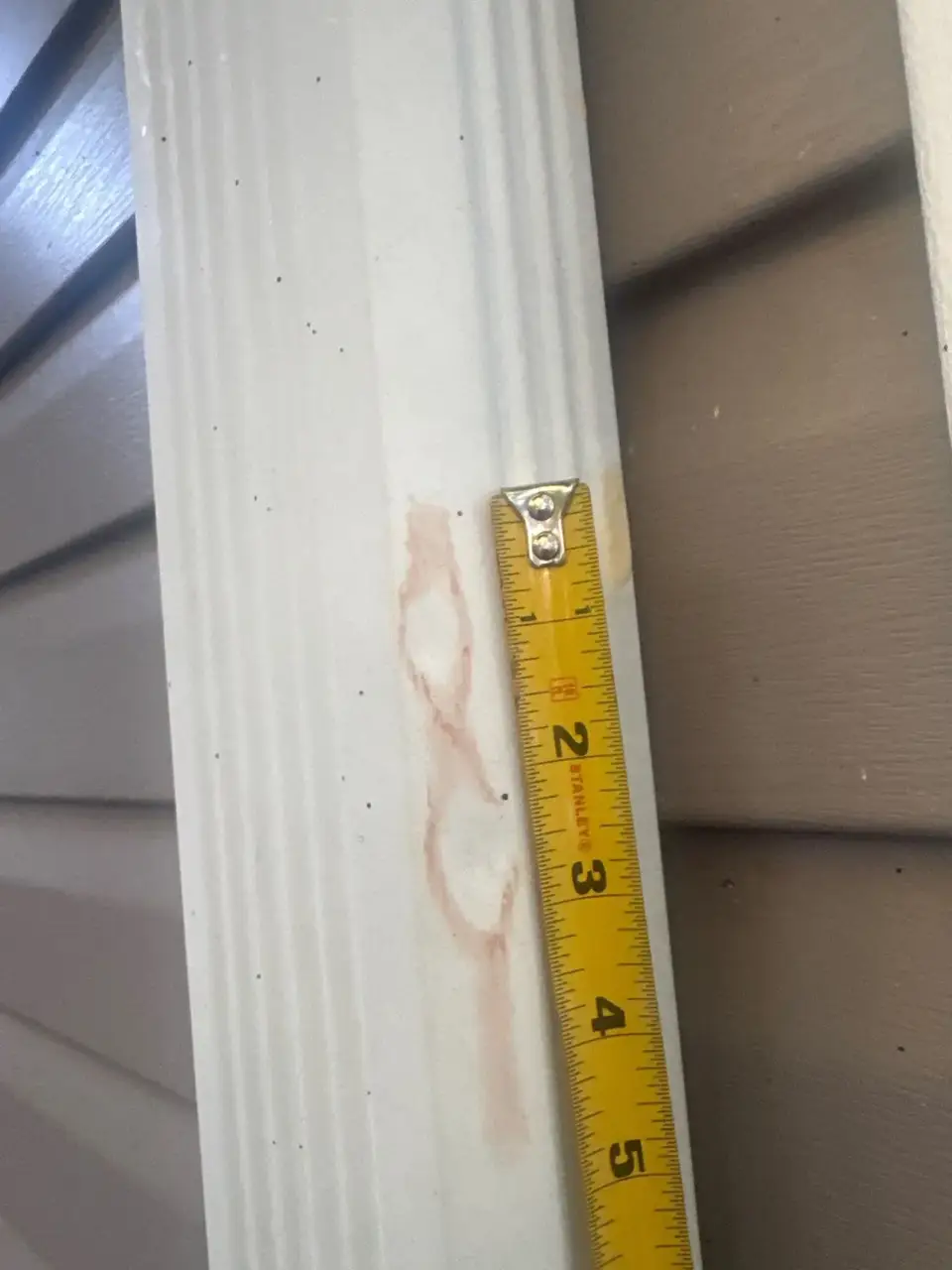 Tape measure rests against white gutter beside tan horizontal siding.