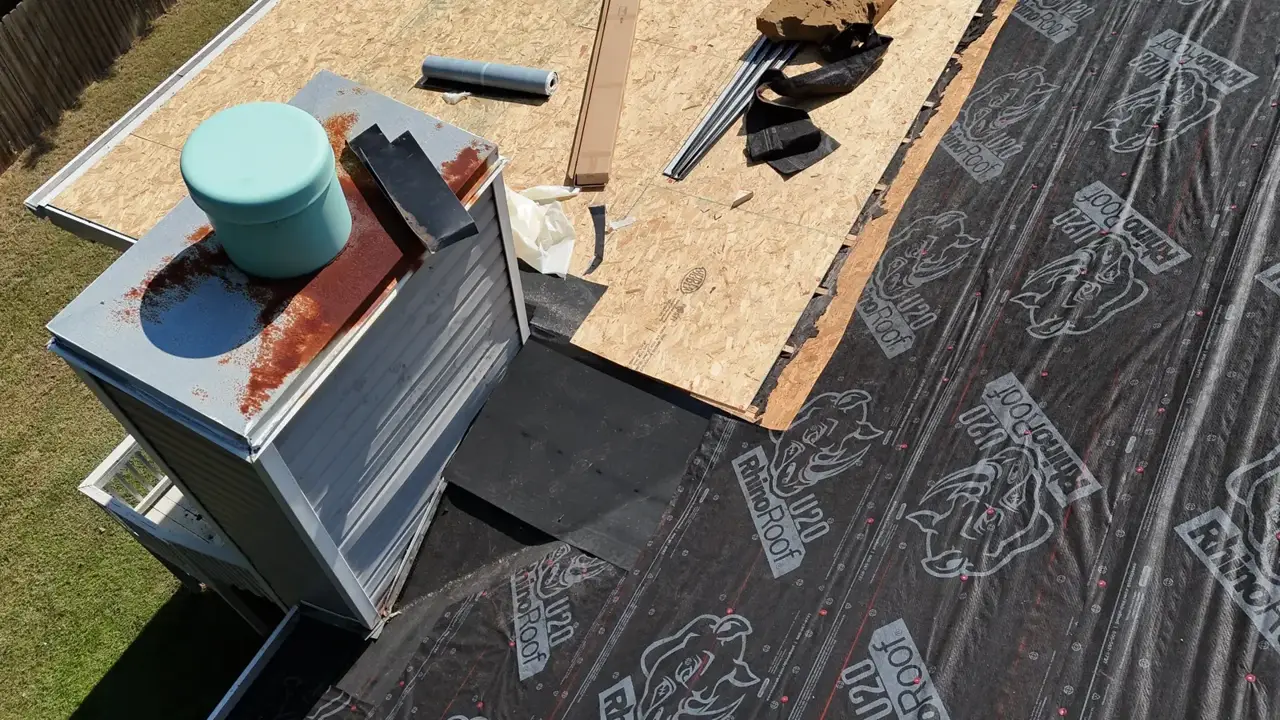 Roof replacement materials surround a chimney, with black underlayment, plywood decking, and metal flashing visible.
