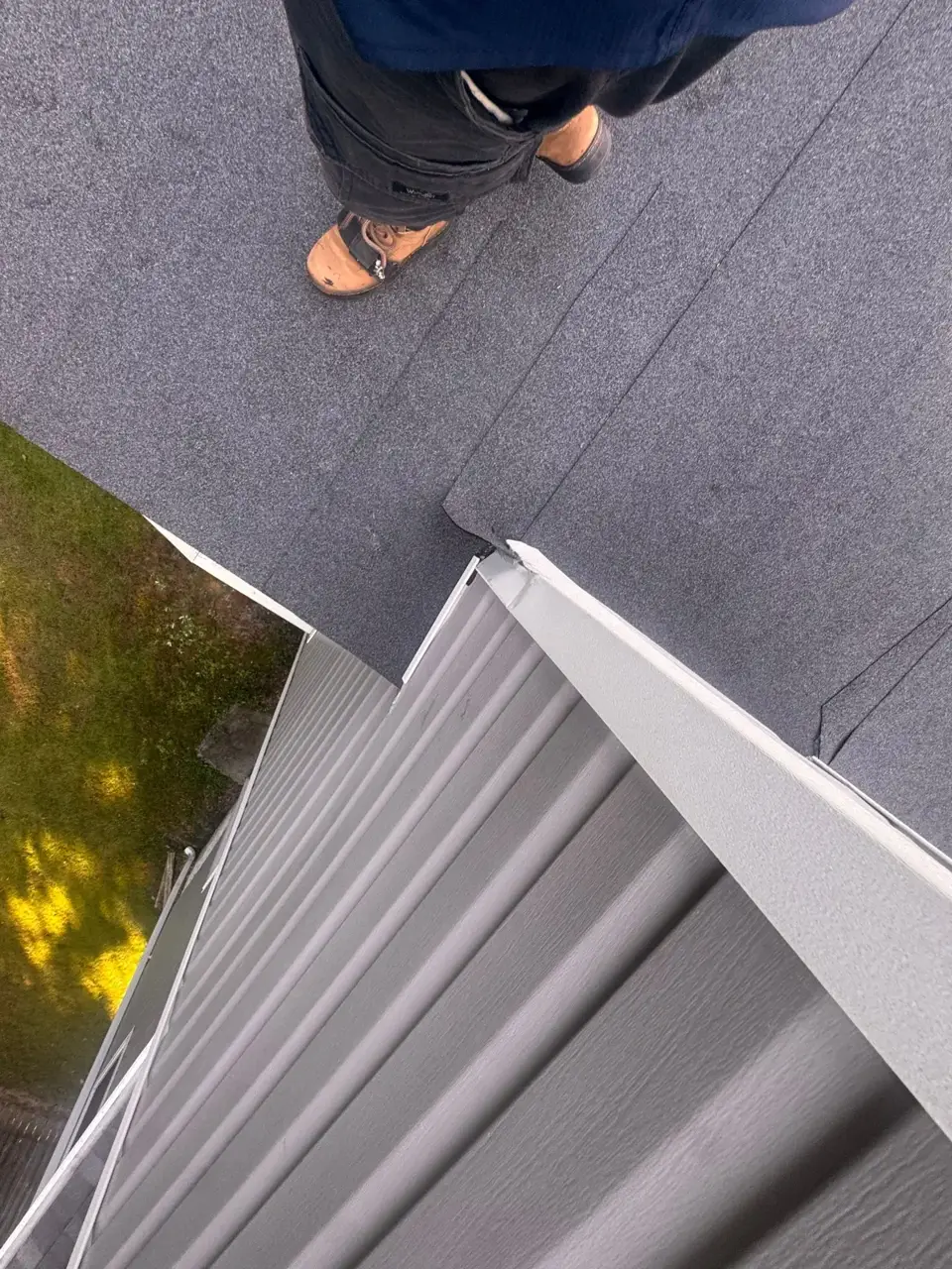 Worker's boots stand on gray roofing near white metal trim and vertical siding in Bethlehem, Georgia.