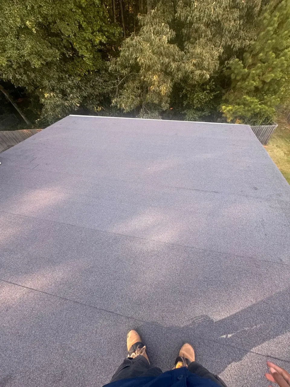 New-looking gray roofing covers a broad flat section, with trees beyond and worker's boots visible.