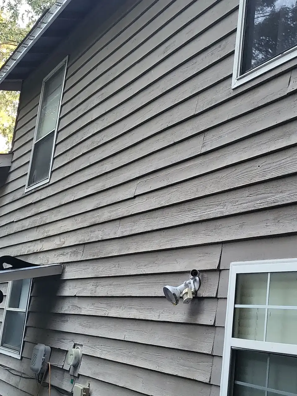 Gray horizontal siding with windows, exterior lights, and utility meters visible at a Conyers GA residence.