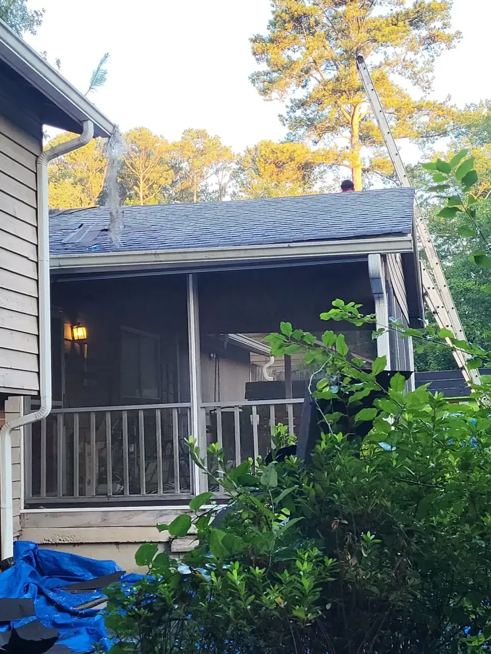 Screened porch with shingled roof, gutter, blue tarp, shrubs, and ladder visible in Conyers GA.