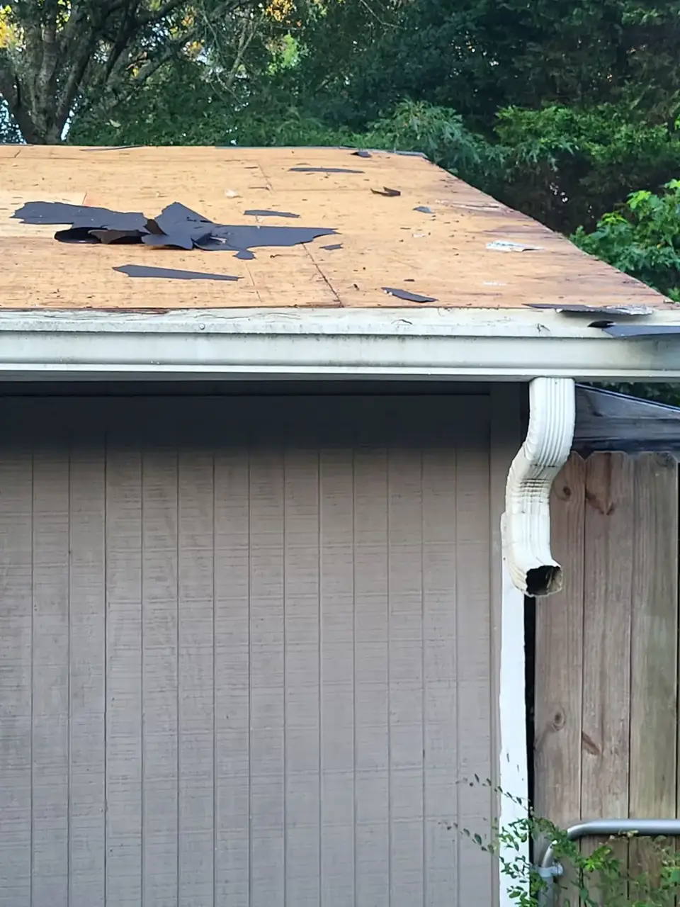 Roof deck with scattered dark remnants above siding, gutter, and downspout in Conyers, GA
