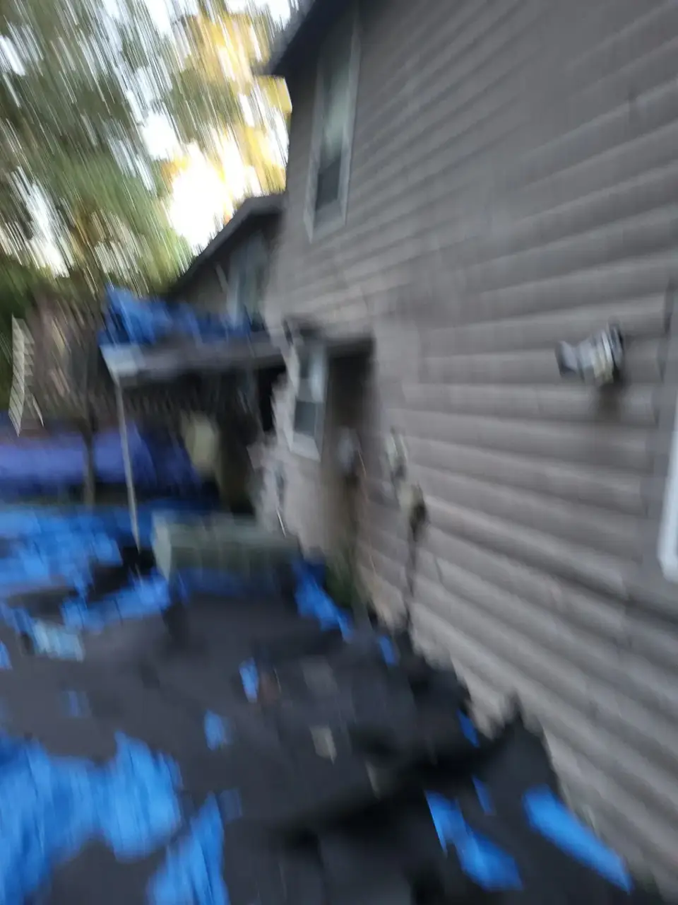 Blurred view of house siding with blue tarps and dark roofing materials in Conyers, GA