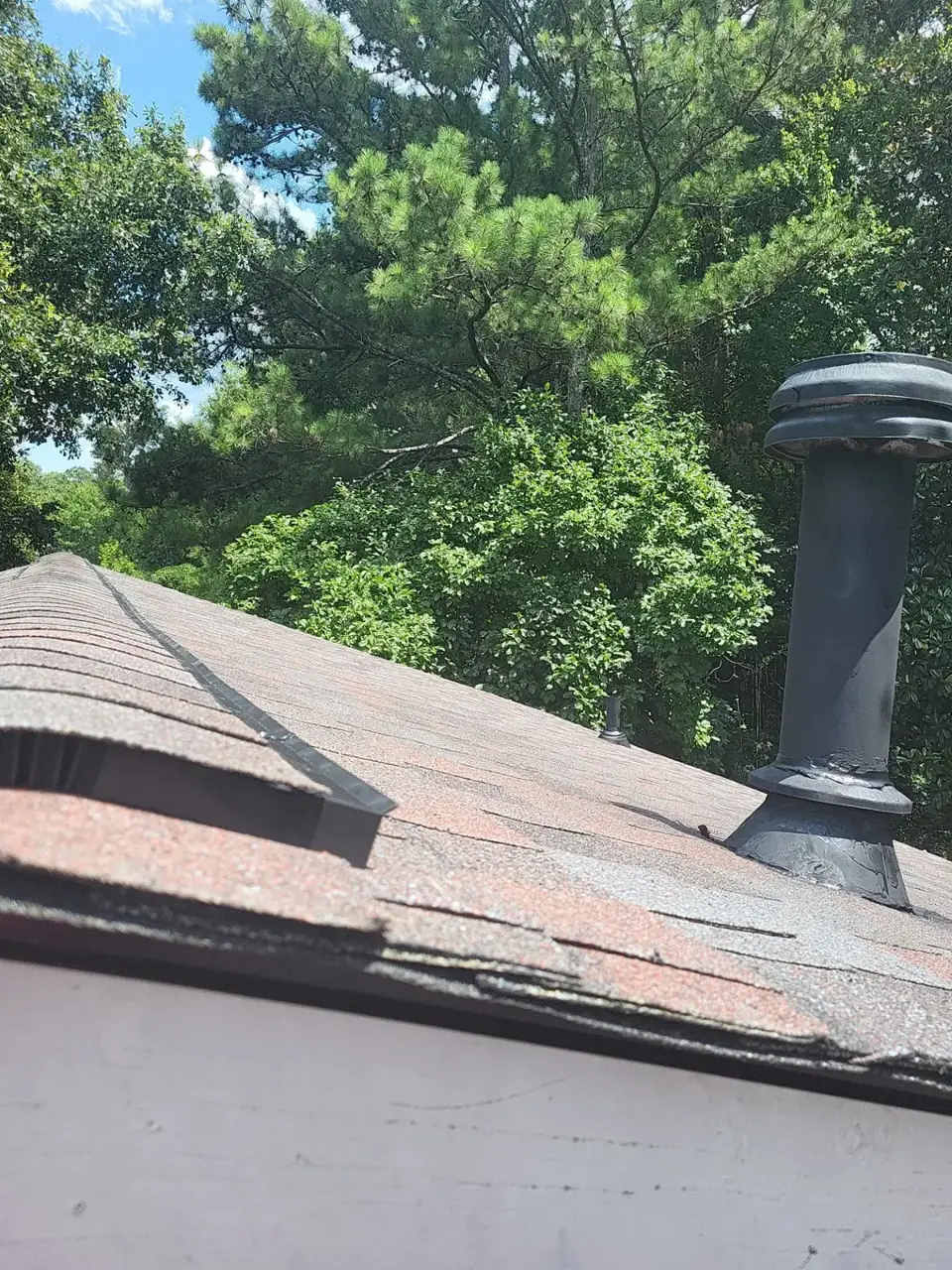 Aged asphalt shingle roof with chimney vent and leafy trees visible in Conyers GA