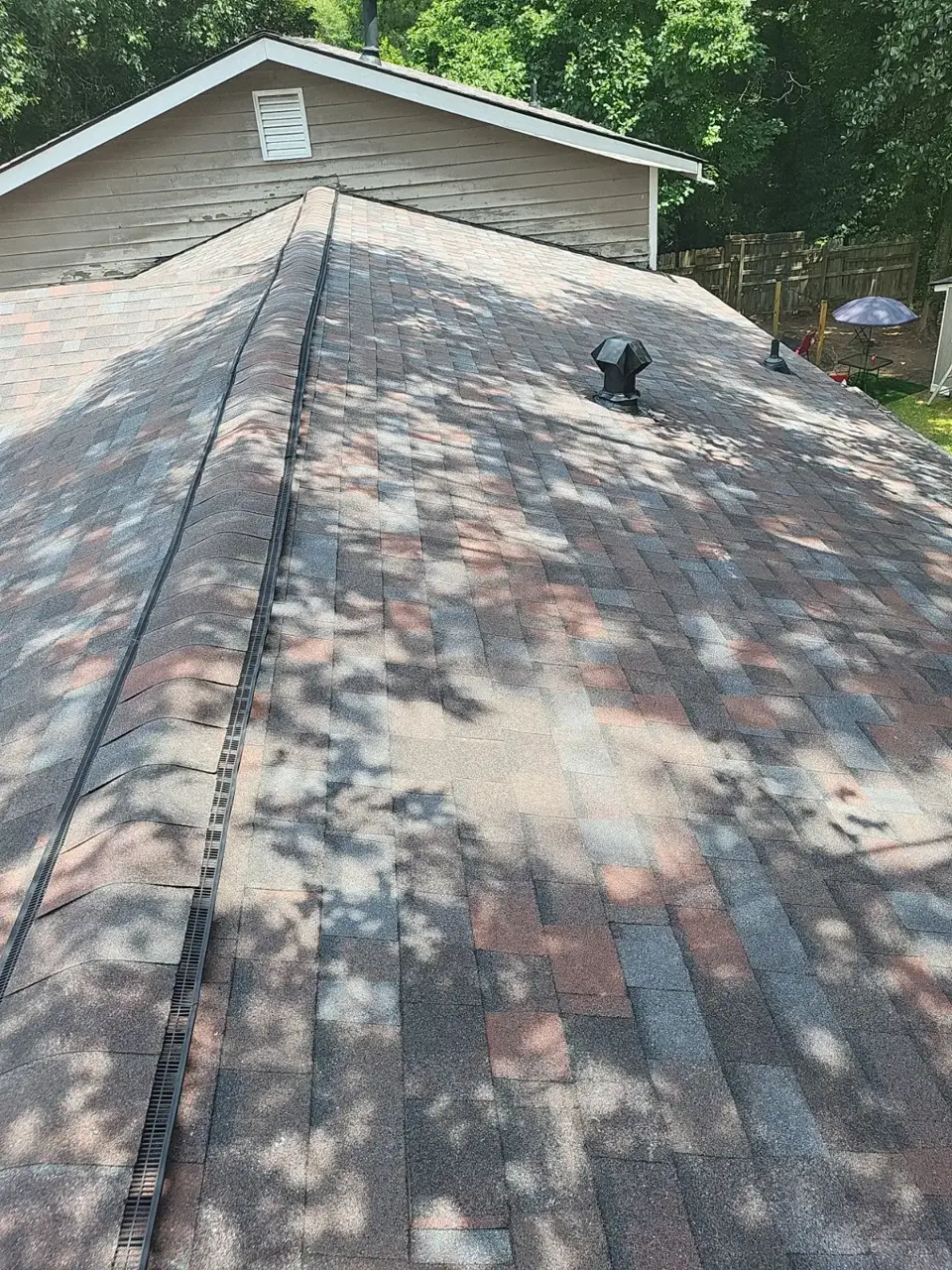 Multicolored shingle roof with ridge vent, roof vents, and wooded surroundings