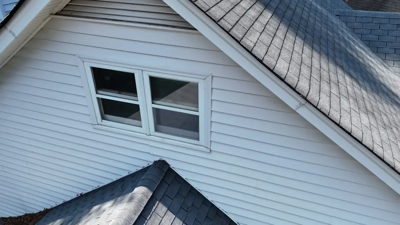 White-sided home gable with two windows and overlapping dark shingle roof sections