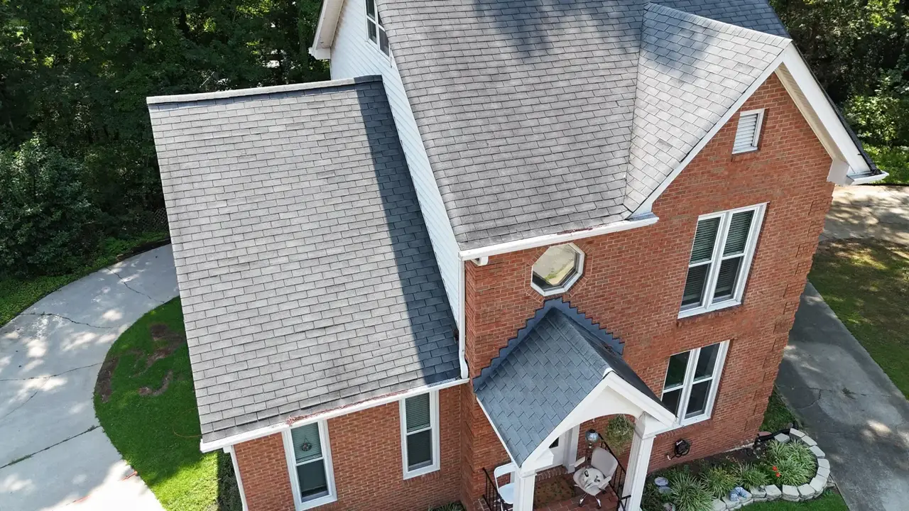 Aerial view shows gray shingle roofs, brick siding, white trim, garage, and landscaping
