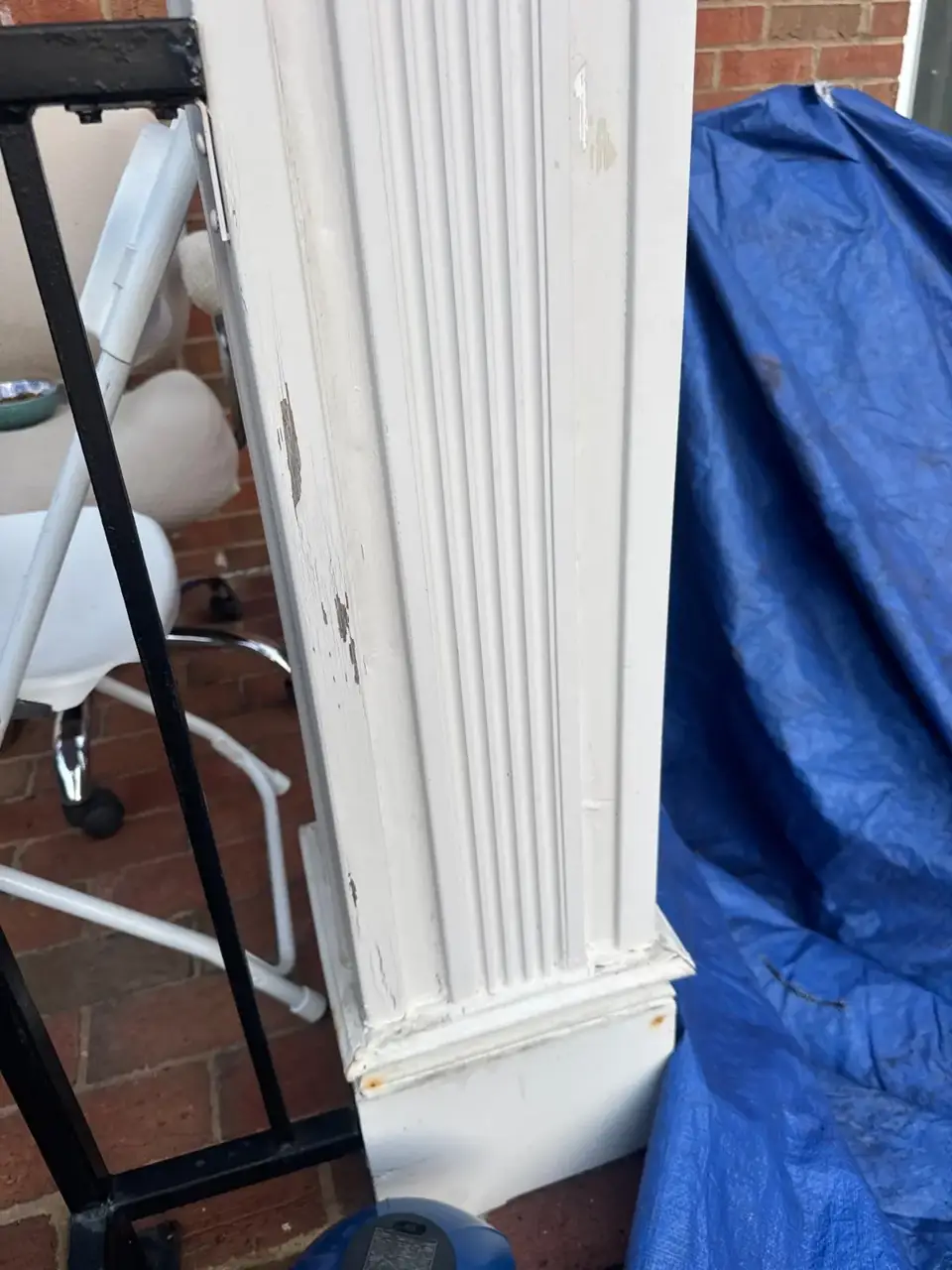 Close-up of worn white porch column beside a blue tarp and metal railing