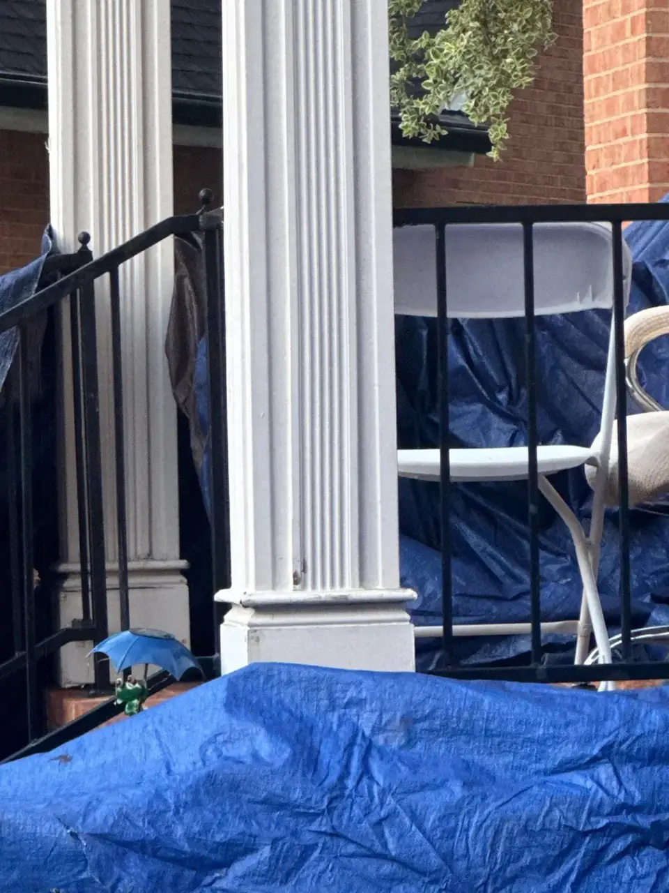 Blue tarp covers a porch railing, white column, and outdoor furniture during roof work.