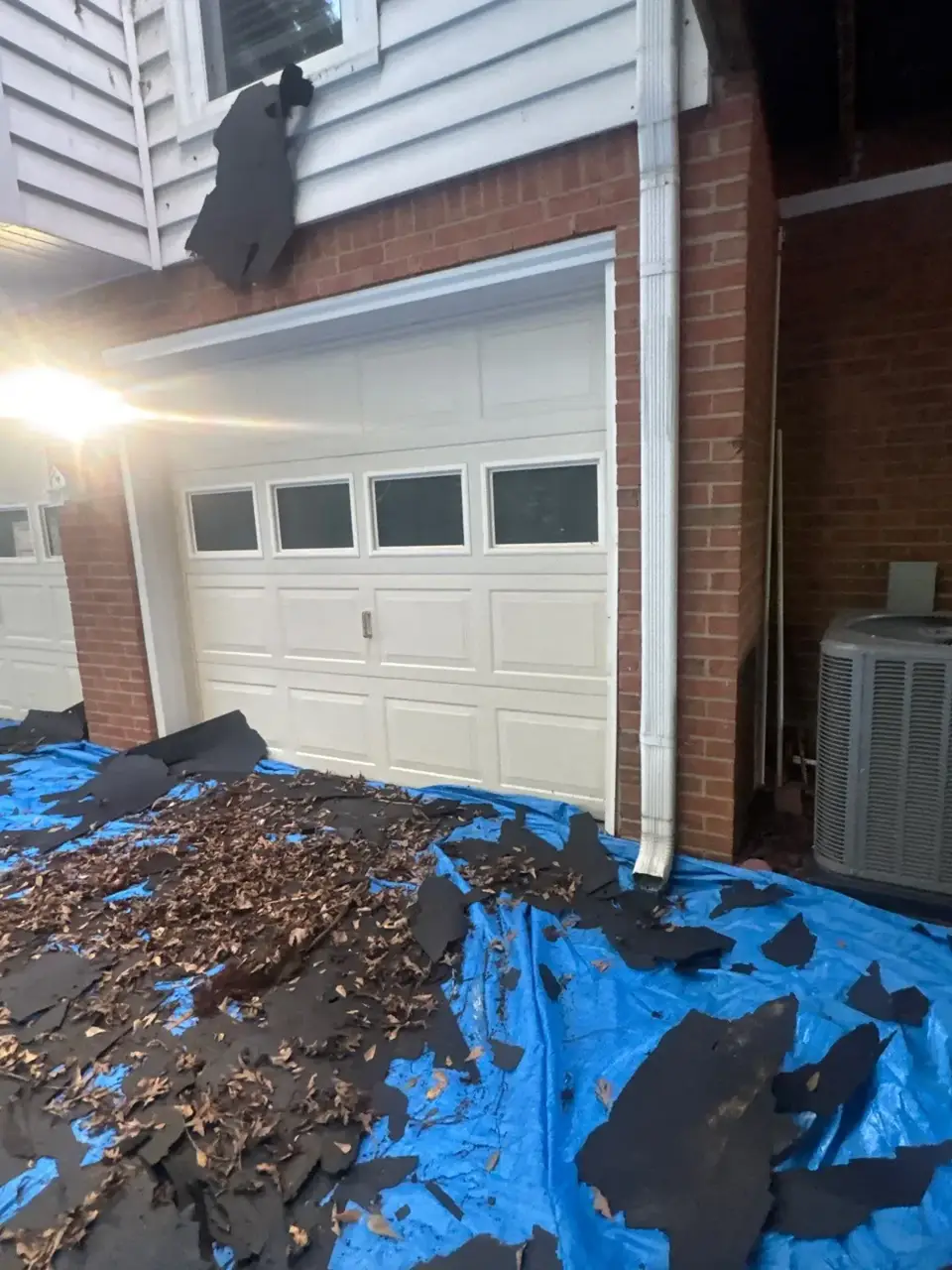 Decatur GA garage exterior with blue tarps, removed roofing debris, leaves, and exposed siding.