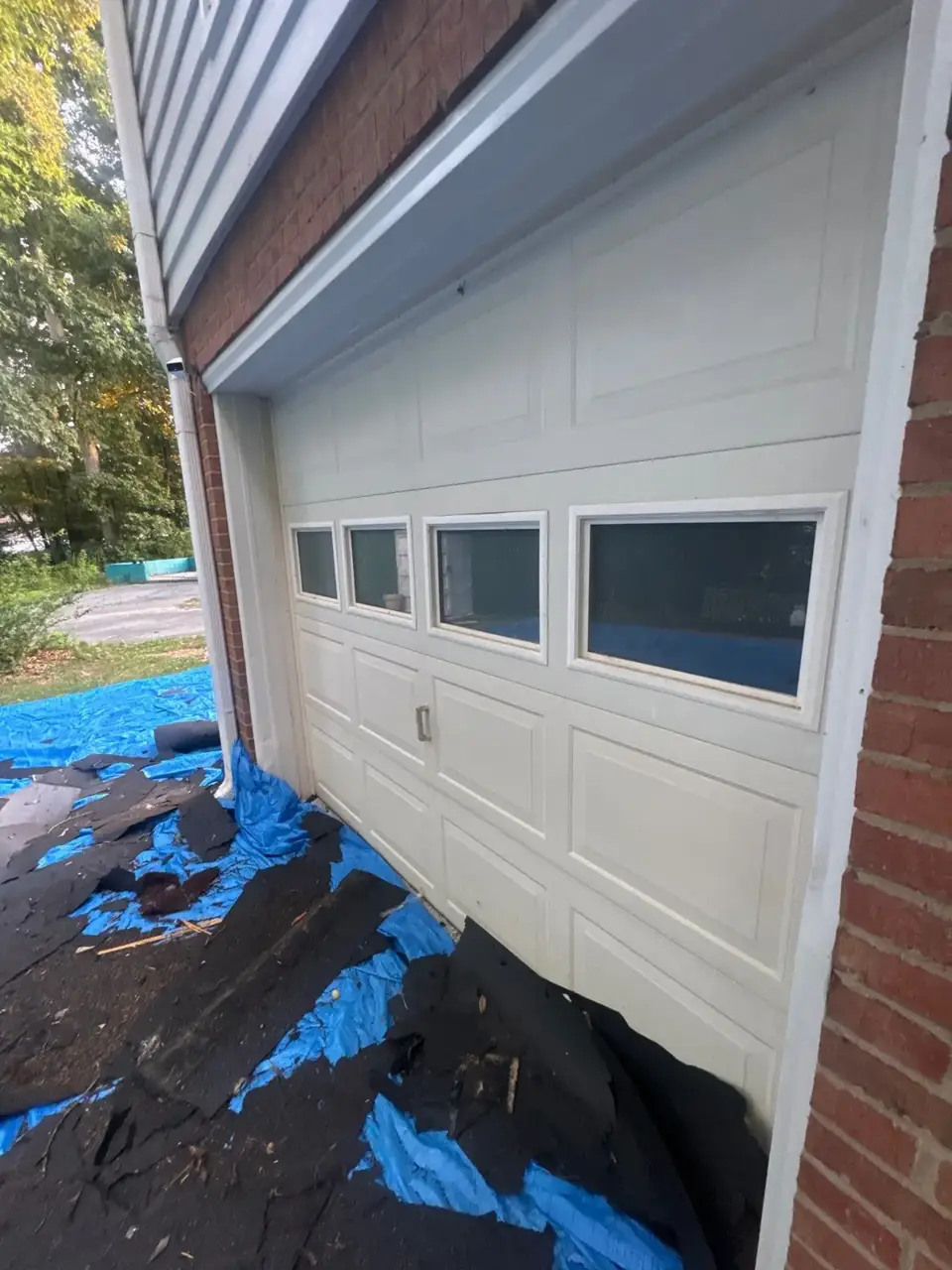 Decatur GA white garage door bordered by brick, with blue tarps and roofing debris.