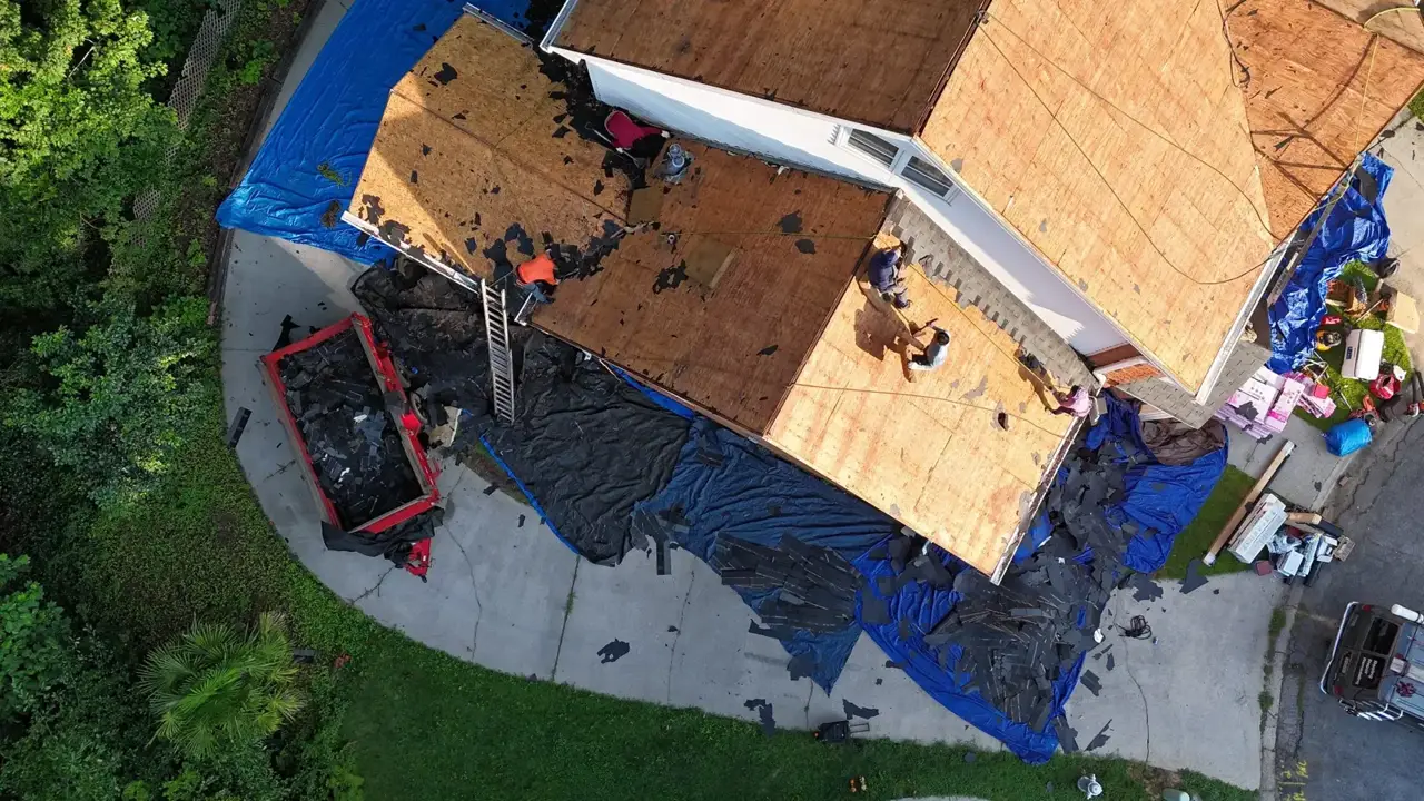 Aerial view of roof replacement with exposed decking, tarps, debris, ladder, and trailer in Decatur GA