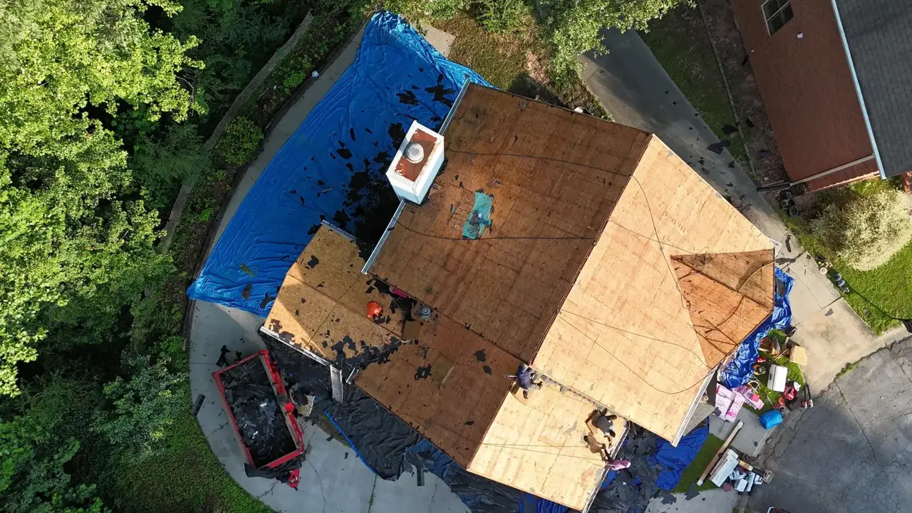 Aerial view of roof replacement with exposed decking, blue tarps, debris, and equipment in Decatur, Georgia