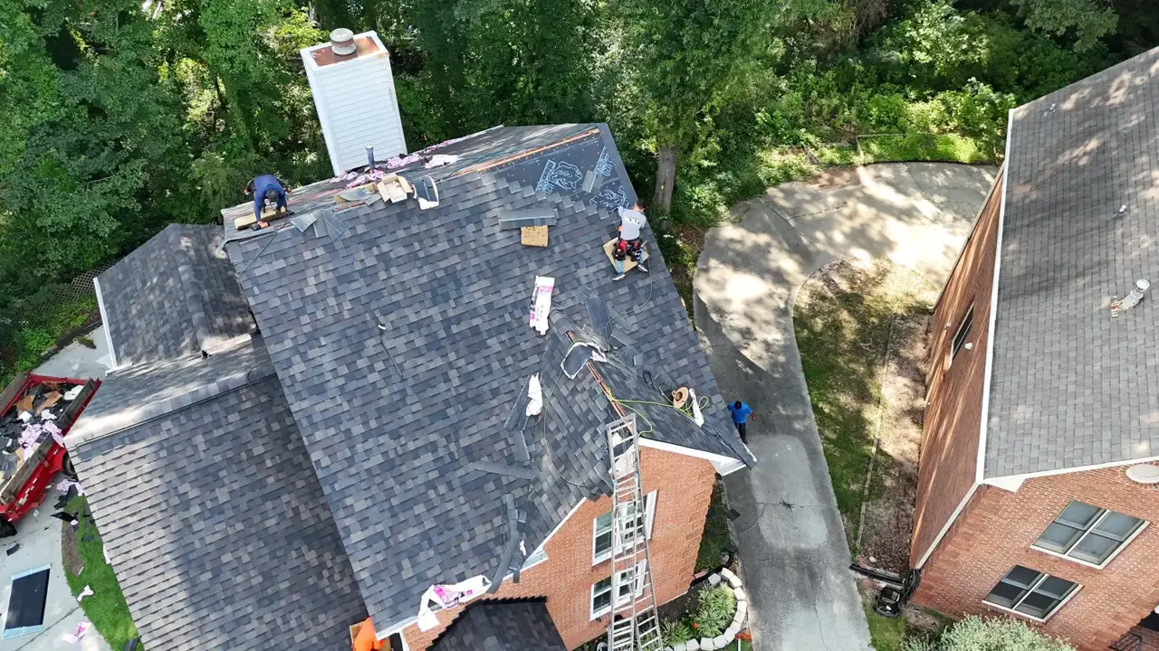 Aerial view of newly shingled residential roof with chimney, ladders, workers, and adjacent driveway