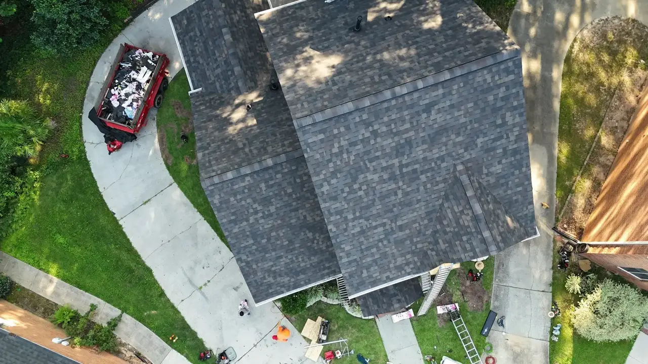 Completed dark shingle roof viewed from above, with debris trailer, ladders, and surrounding residential property in Decatur, Georgia