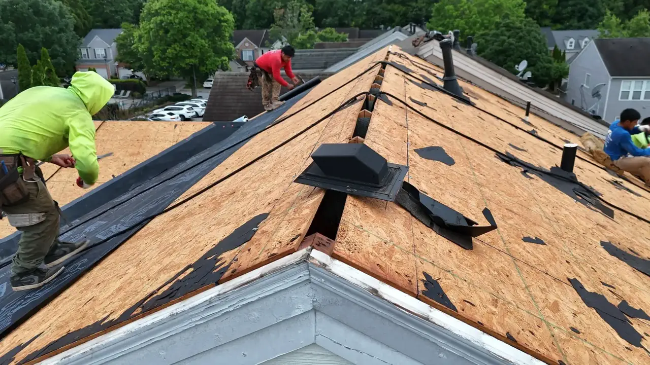Roof replacement underway with workers, exposed decking, vents, and neighboring homes