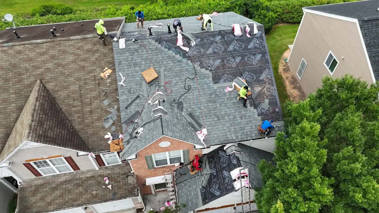 Aerial view shows roof replacement work with workers, exposed underlayment, shingle bundles, and existing roofs in Duluth GA.