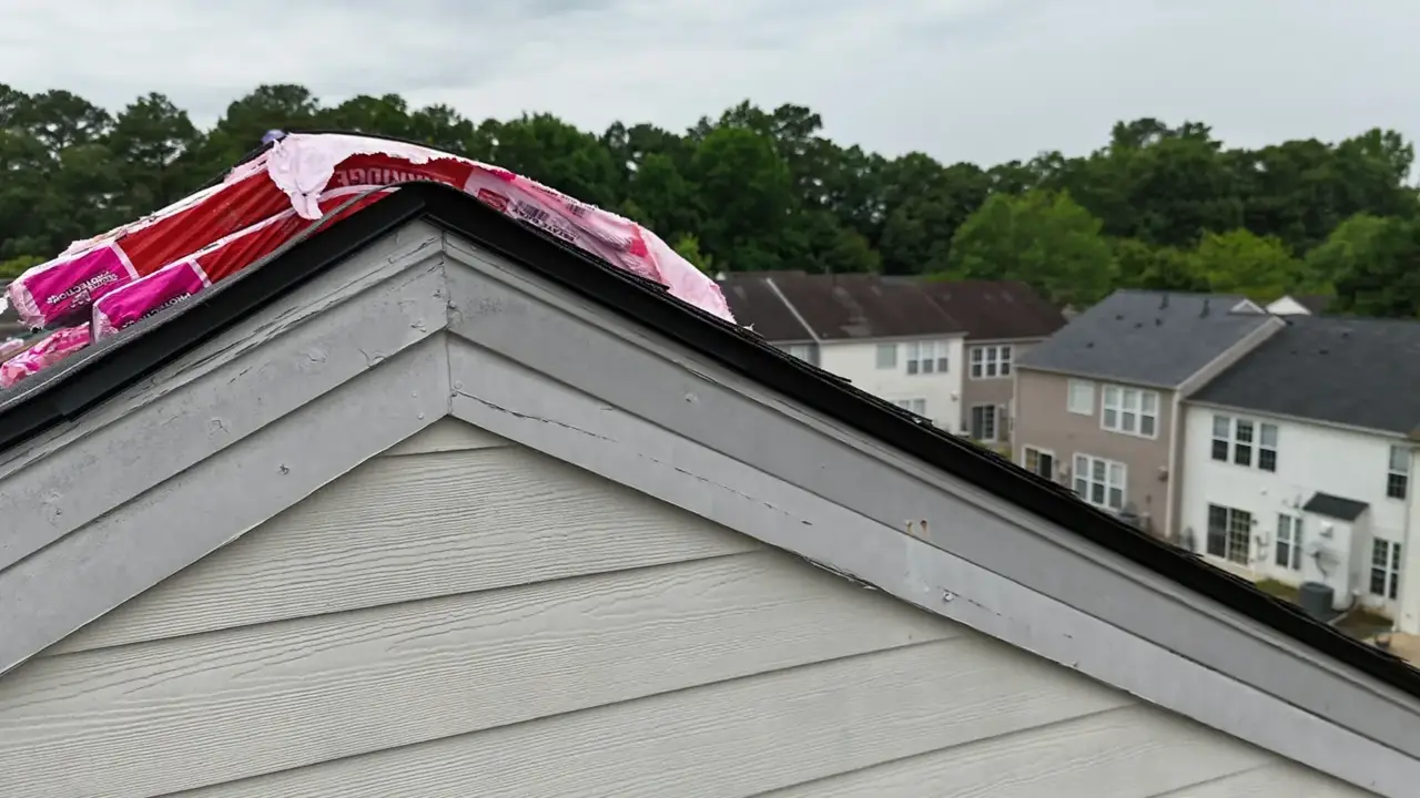 Roof gable with exposed pink underlayment above gray siding in Duluth, Georgia