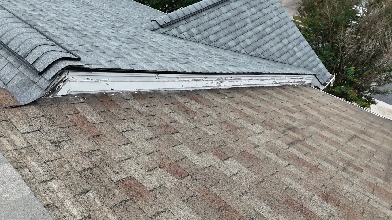 Weathered roof shingles meet a newer gray shingle section along exposed flashing