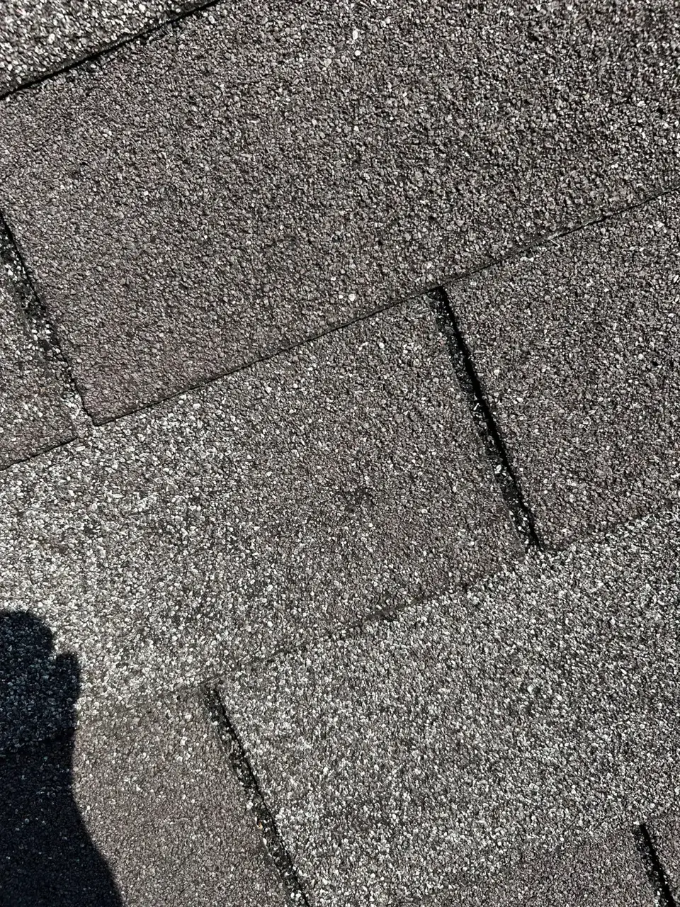 Close-up of weathered gray asphalt shingles showing overlapping rows and dark seams