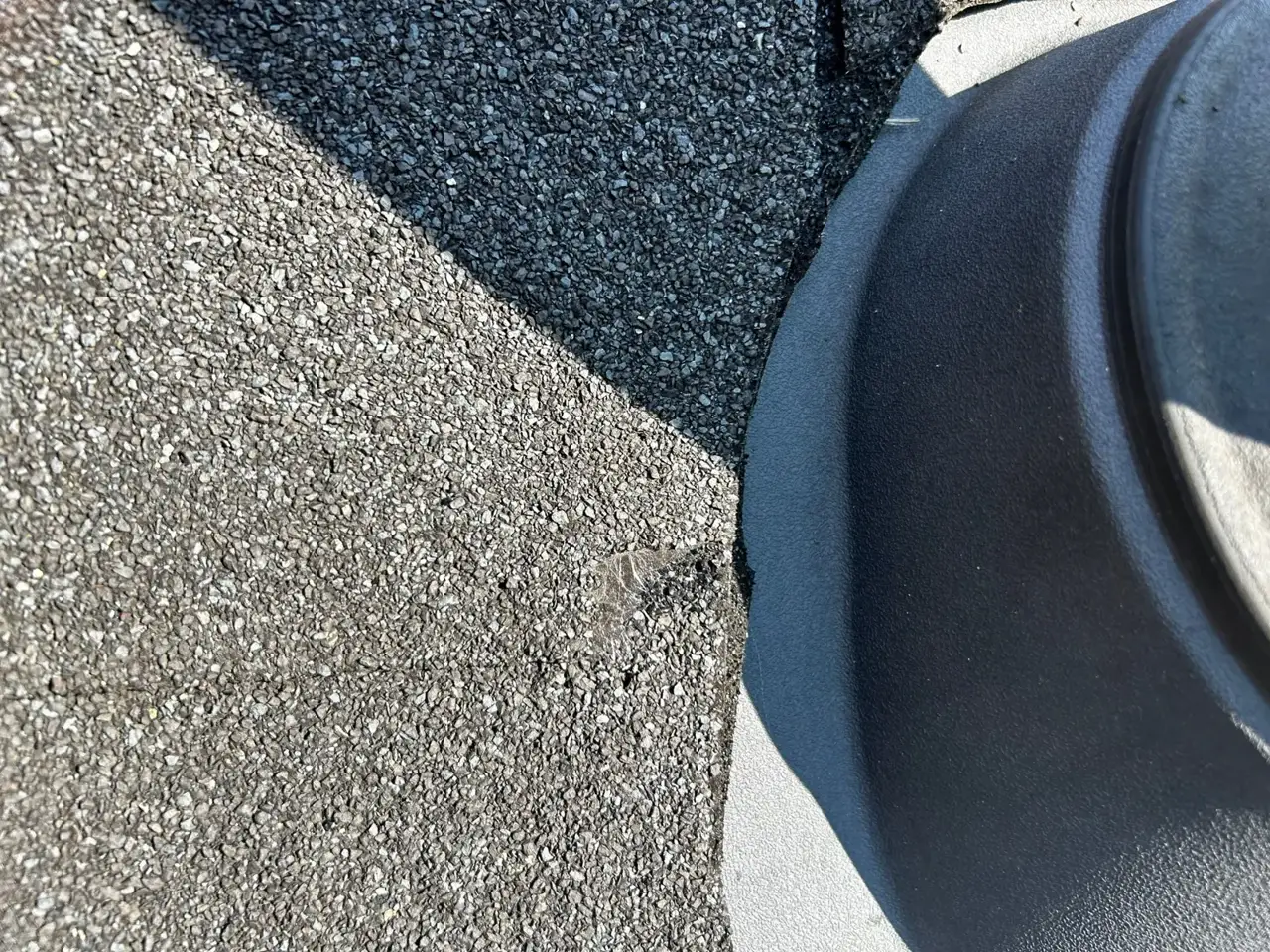 Asphalt shingles meet a black roof vent flashing in close-up at a roof penetration