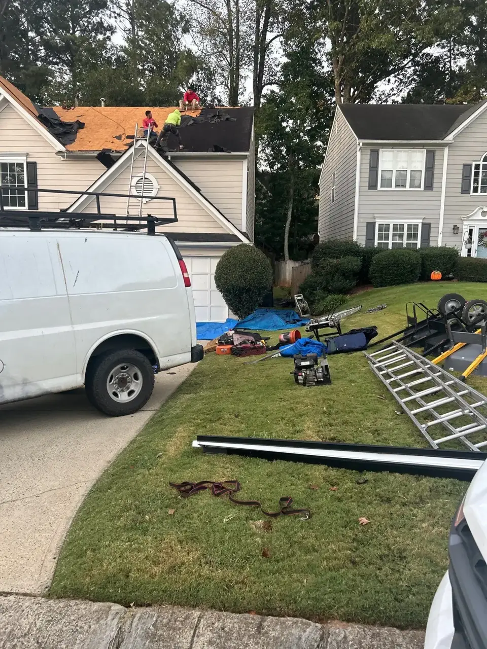 Roof replacement scene in Kennesaw GA with workers, exposed decking, tools, ladders, and tarp.