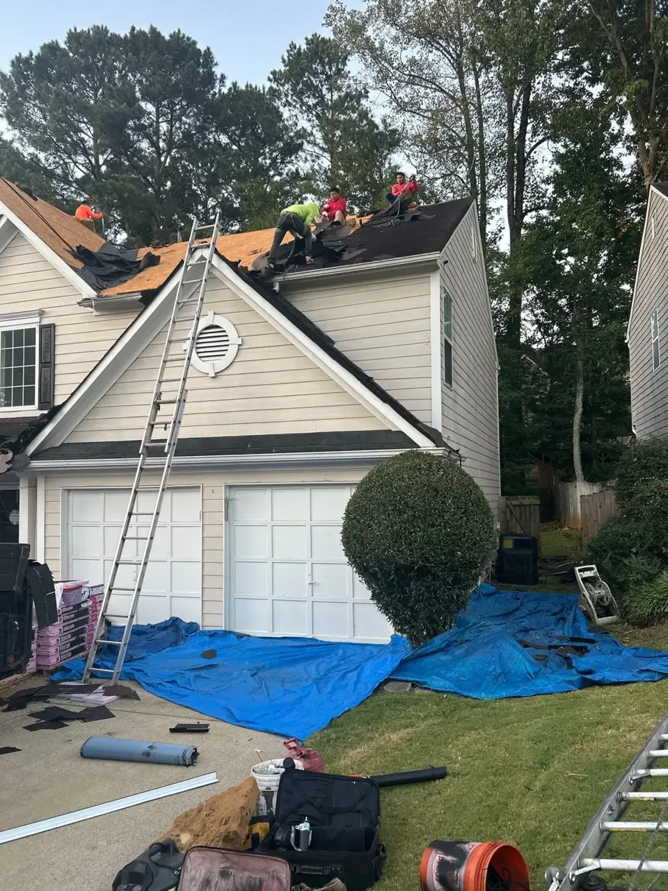Roof replacement underway with workers, ladders, tarps, and exposed roof decking in Kennesaw GA