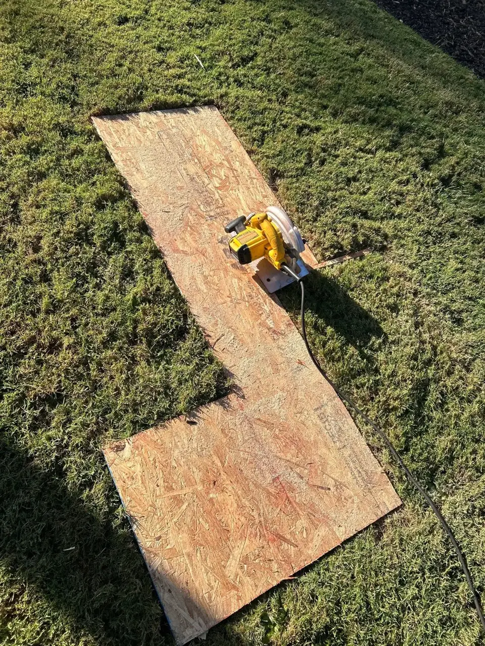 Two plywood boards and a yellow circular saw rest on grass