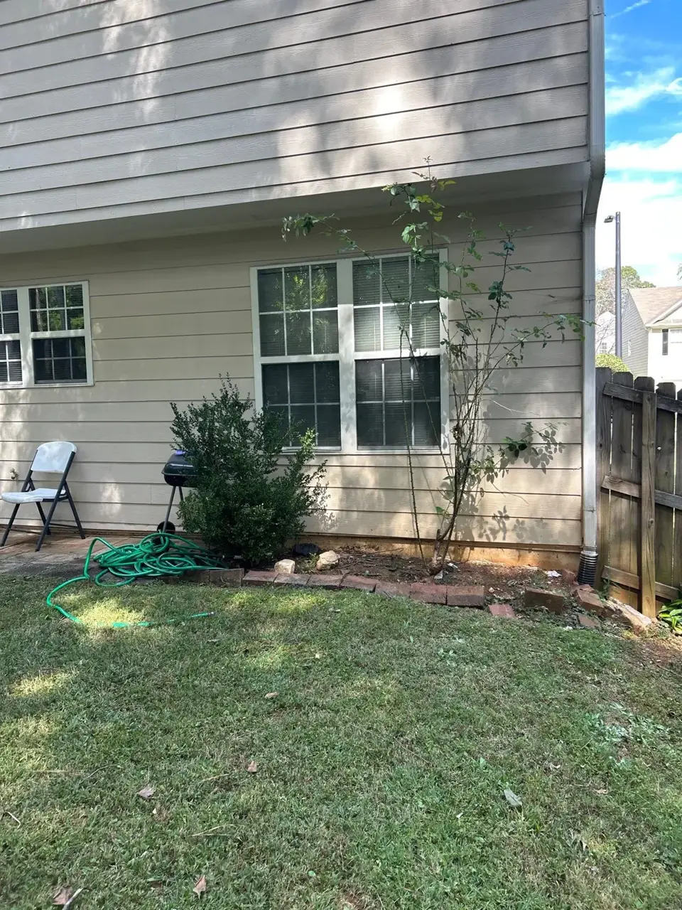 Residential home's siding, windows, downspout, garden hose, and lawn visible beside a wooden fence in Kennesaw GA.