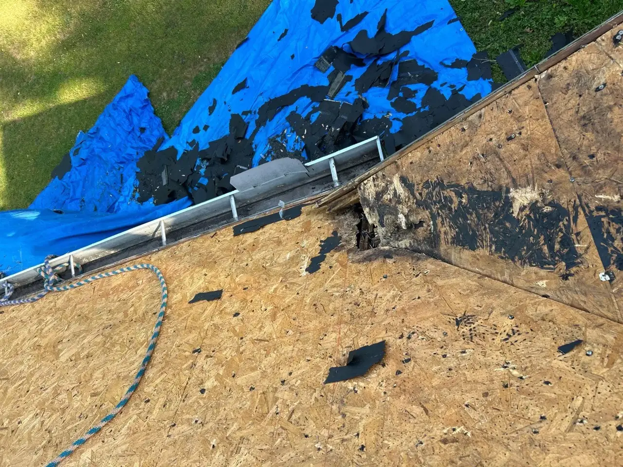 Roof decking and gutter edge overlook a blue tarp covered lawn in Lawrenceville GA.
