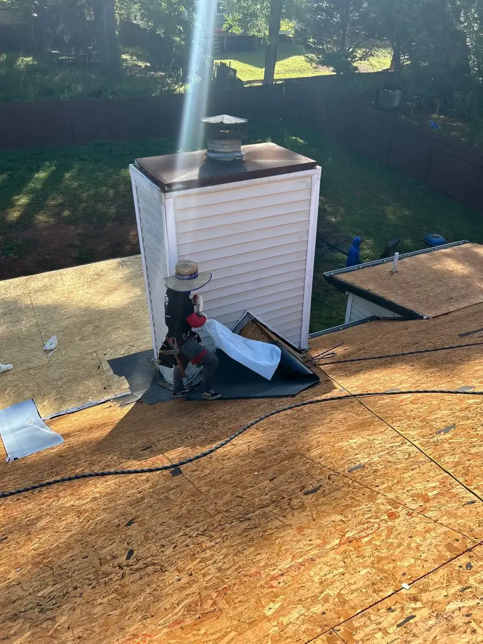 Worker installs roofing materials around a chimney on exposed decking in Lawrenceville GA